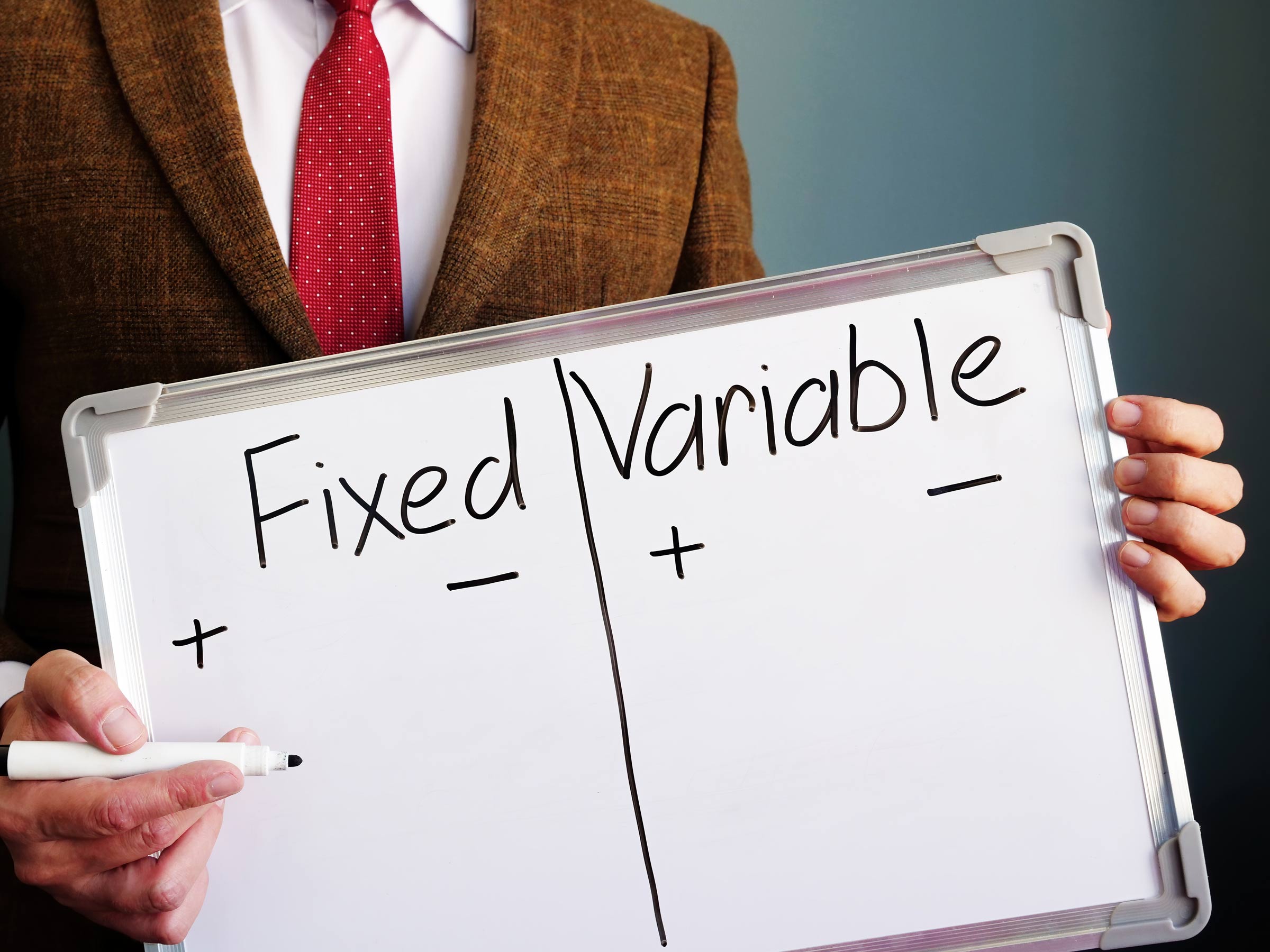 Man holding a marker white board with Fixed and Variable columns written on it in black